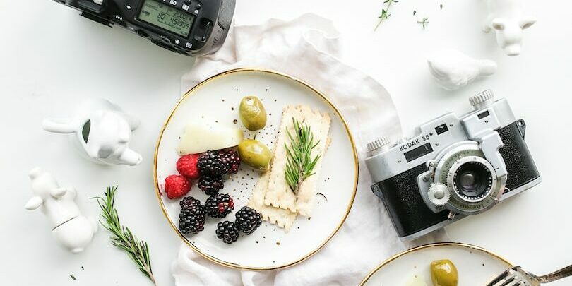 three assorted cameras near fruits and ceramic figurines