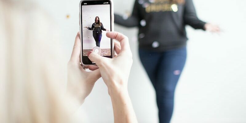 person holding white smartphone taking photo of woman wearing blue jeans