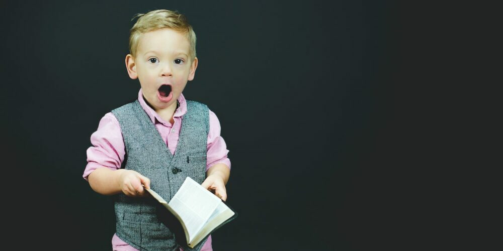 boy wearing gray vest and pink dress shirt holding book