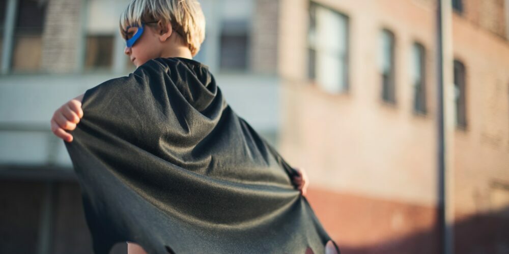 selective focus photography of boy wearing black Batman cape